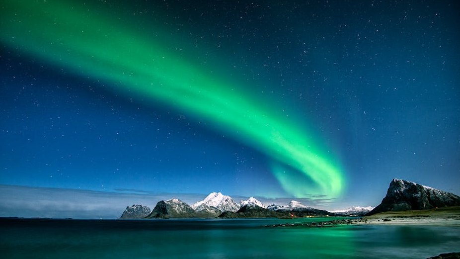 northern lights over Lofoten Islands in Norway with mountain peaks and wooden cabins in the foreground