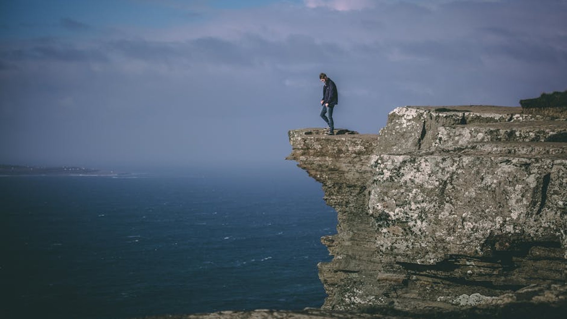person standing alone on a cliff edge overlooking a vast natural landscape with sunrise in the background